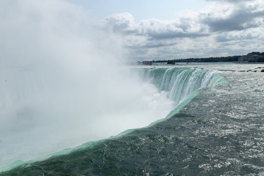 Niagara Falls, Canada - Turquoise water rushes over the edge of Horseshoe Falls with dramatic mist rising above the cascade