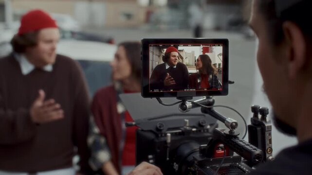 Professional cinematographer filming scene with actors on outdoor movie set after female assistant slating clapperboard. Professional digital camera rig with external monitor in foreground