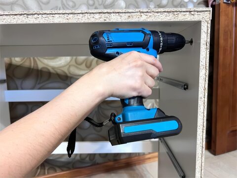 Hand using blue cordless drill to assemble white furniture