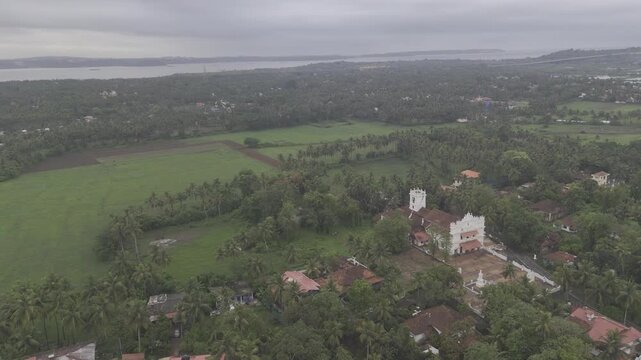 Aerial landscape view of Talaulim fields during the monsoon season, showcasing lush greenery, coconut palm trees, the Zuari River, and dramatic cloudy skies across the tropical countryside of Goa