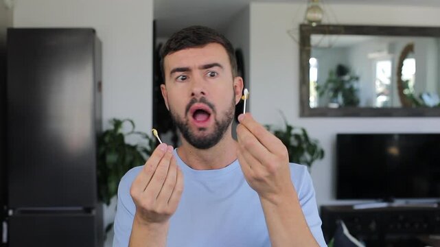 Shocked Man Looking At Earwax On Cotton Swab Inside Bathroom After Cleaning Routine
