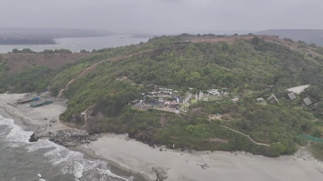 Aerial view of a coastal cliff near Dream Beach in Chapora, Goa, overlooking the Chapora River and the Arabian Sea, showcasing rugged terrain, lush vegetation, and scenic tropical landscapes.