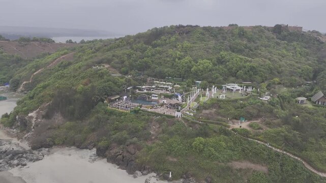 Aerial view of a coastal cliff near Dream Beach in Chapora, Goa, overlooking the Chapora River and the Arabian Sea, showcasing rugged terrain, lush vegetation, and scenic tropical landscapes.