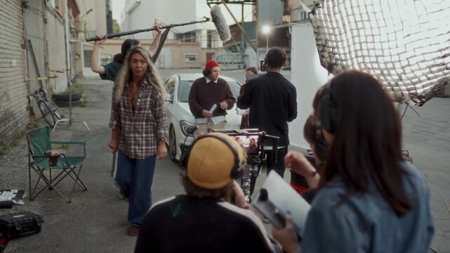Behind the scenes view of team of young filmmakers reviewing and discussing live take on camera monitor while shooting scene in outdoor urban alley