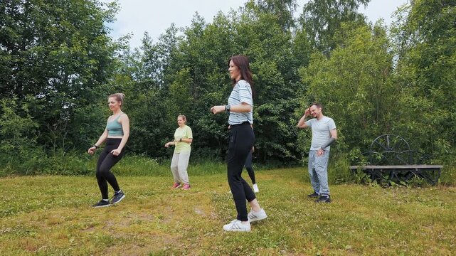 Group of adults dancing and jumping in a park, enjoying an outdoor dance fitness session