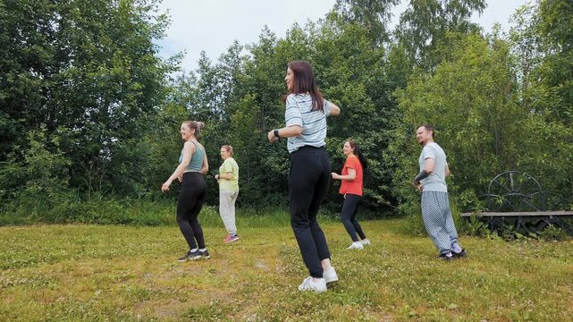 Group of adults dancing and jumping in a park, enjoying an outdoor dance fitness session
