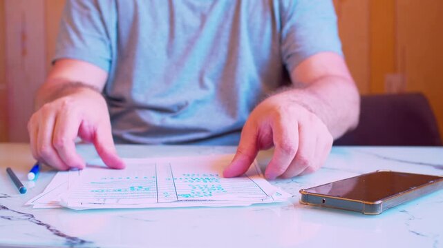 Low angle close-up of man stacking paper documents and starting to write. Blurred silhouette in home office.Natural light. Metaphor for business organization, efficiency and new project.