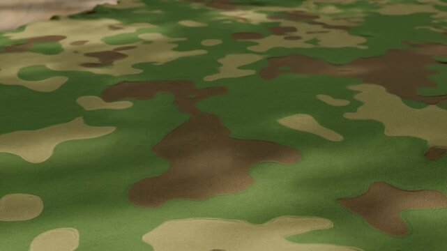 Slow pan close up of camouflage fabric rippling across textured cloth on studio tabletop with subtle waves and shifting soft shadows
