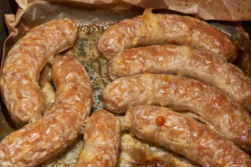 Fototapeta premium Hot homemade sausages with a juicy texture and golden surface on a parchment-lined baking tray. Golden Brown Pork Sausages Fresh from the Oven. Baked Homemade Sausages Close Up.