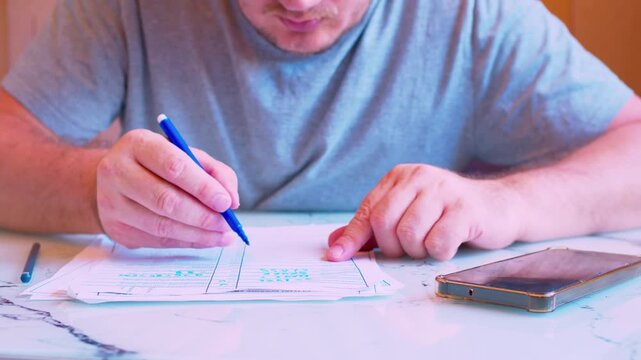 Low angle close-up of a man's hands filling out a paper document with a marker. Cinematic shot of a  man carefully writing with a felt tip pen on a form or contract under natural light.