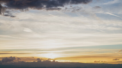 Fototapeta premium Panoramic view of a dramatic sunset sky with layered clouds illuminated by warm golden light. Atmospheric evening landscape featuring colorful cloud formations, soft sunlight and a distant horizon. Pe