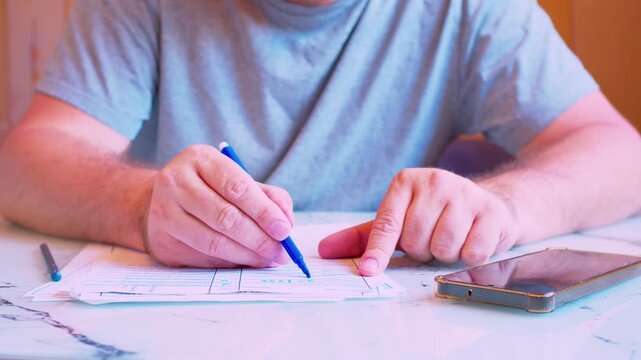 Low angle close-up of a man's hands filling out a paper document with a marker. Cinematic shot of a  man carefully writing with a felt tip pen on a form or contract under natural light.