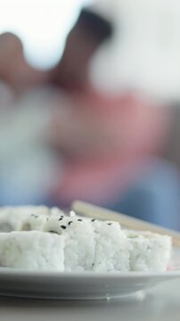 Closeup, food and sushi in home with chopsticks, culinary and couple with seafood cuisine. People, plate and rice at house with ginger, Japanese dish and raw fish nutrition for authentic delicacy
