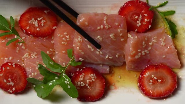 Salmon sashimi with fresh strawberry slices and sesame seeds, close up. Top view of salmon carpaccio or sashimi served with strawberry slices rucola and chopsticks
