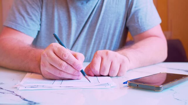 Cinematic shot of writing with a pencil on a document at home. Defocused background, soft window light. Visualizes tax preparation, editing agreement, family budget audit and making corrections.