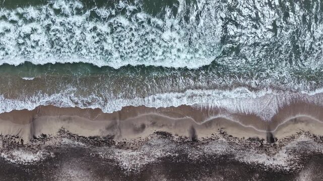 The ocean waves wash onto the shore as the day comes to an end. The beach shows sand patterns shaped by the water. Birds might be seen nearby.