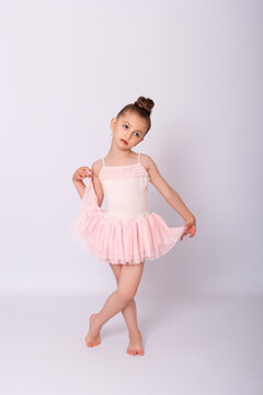 Beautiful little child in ballet dress standing cross-legged and holding her pink tutu skirt.