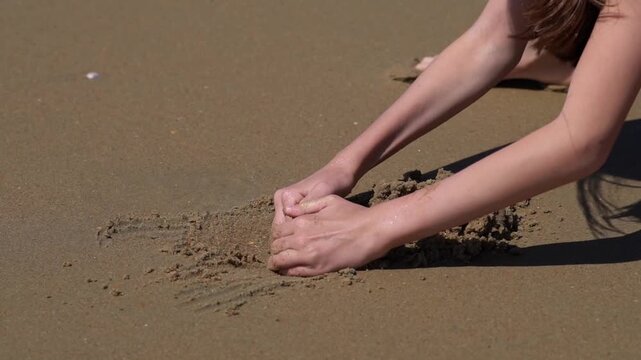 Close up of small child hand engaged in creative play digging wet sand and mud during summer beach vacation displaying playful focus on raw earth texture and natural craft