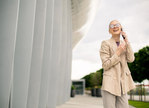 Woman talking on the phone and smiling outside a modern building during the day