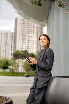 Woman stands by a large planter with a tablet in a modern urban setting
