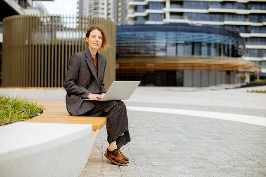 Woman working on laptop outside modern building in urban setting during daytime