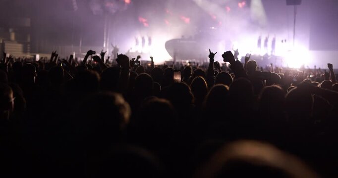 Silhouetted concert audience cheering with raised fists and heavy metal horn hand gestures during a live music performance.