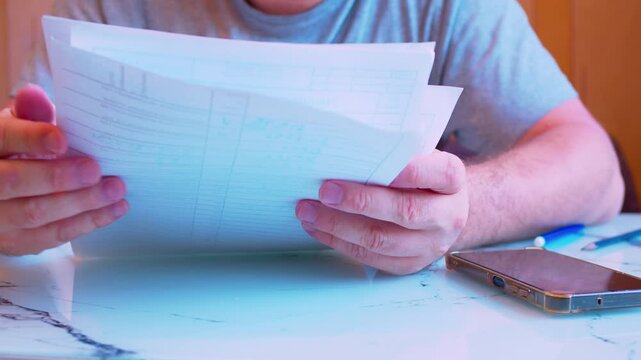 Cinematic closeup shot of browsing paperwork on a desk at home. Defocused background, soft window light. Visualizes billing management, family budget planning, home bureaucracy and searching files.