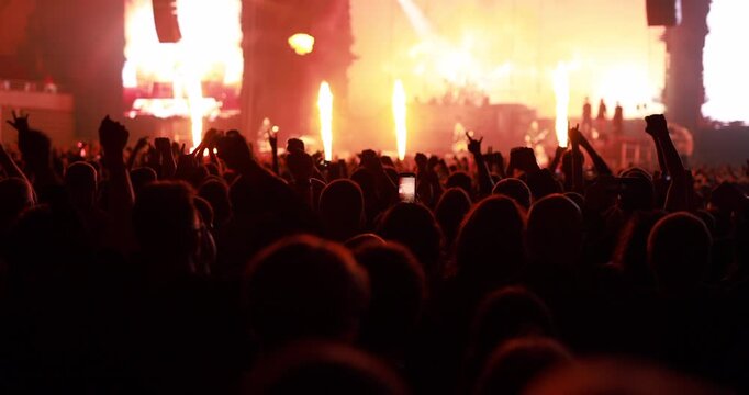 Silhouetted crowd raising hands and fists in celebration during an outdoor music festival with intense orange illumination.