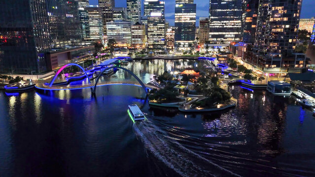 Aerial drone view of Perth Elizabeth Quay and pedestrian bridge illuminated at night with reflections