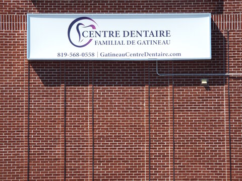 Gatineau, Quebec, Canada &ndash; May 10, 2026: A white sign for the "Centre Dentaire Familial de Gatineau" dental clinic is mounted on a red brick building wall on Bd de l'H&ocirc;pital.
