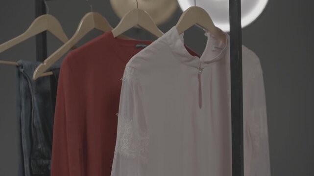 Clothes of various styles hang neatly on wooden hangers on a shelf inside the boutique display window of a modern clothing store.