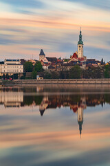 Fototapeta premium Historic center of Tabor with the Church of the Transfiguration reflected in Jordan Reservoir during colorful sunrise. Long exposure cityscape in South Bohemia, Czech Republic.