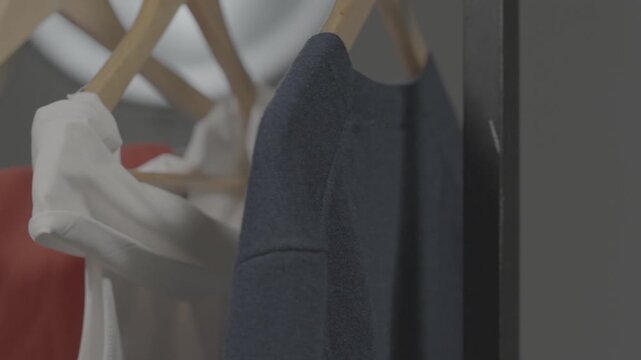 Clothes of various styles hang neatly on wooden hangers on a shelf inside the boutique display window of a modern clothing store.