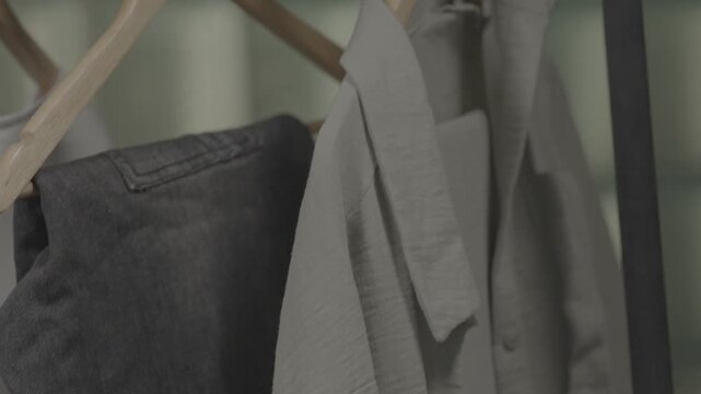 Clothes of various styles hang neatly on wooden hangers on a shelf inside the boutique display window of a modern clothing store.