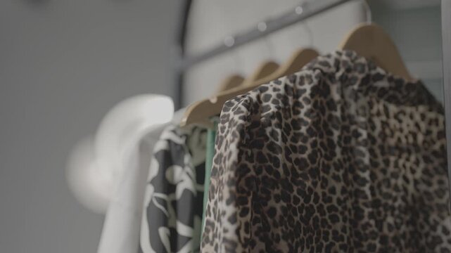 Clothes of various styles hang neatly on wooden hangers on a shelf inside the boutique display window of a modern clothing store.