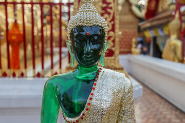 A striking emerald green Buddha statue adorned with a golden robe and red jewels stands serenely at Wat Phra That Doi Suthep in Chiang Mai, Thailand. © Zenstratus