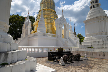 The golden stupa of Wat Suan Dok in Chiang Mai, Thailand, stands majestically against a blue sky with clouds. This Lanna-style temple is a significant religious site. © Zenstratus