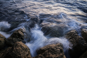 Fototapeta premium Artistic Long Exposure Photography of Rushing Ocean Waves Crashing Over Rugged Dark Coastal Rocks at Twilight