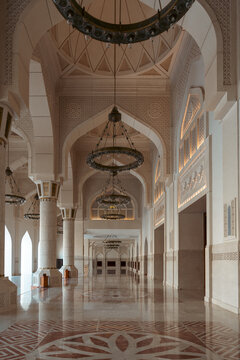 Architectural interior with ornate chandeliers, columns, arches, reflective marble floor, and decorative patterns.