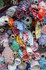 Fototapeta premium A vibrant assortment of fabric rolls, featuring floral, striped, and patterned designs, are neatly stacked in a market stall in Chiang Mai, Thailand