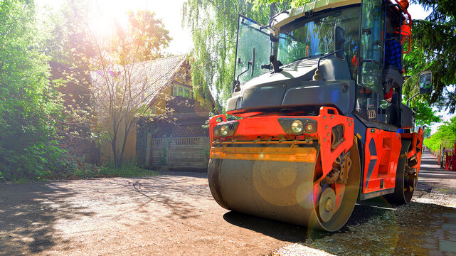 An orange road roller compactor freshly laid asphalt on a new suburban street during daytime.