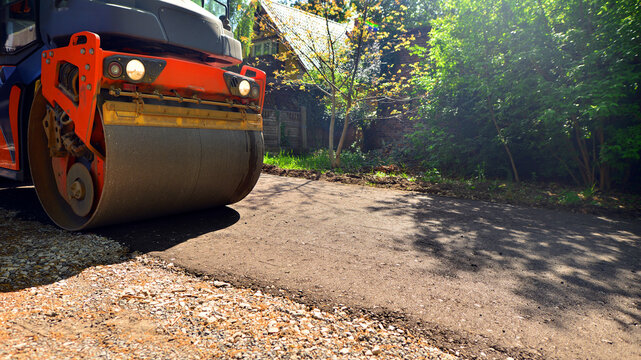 An orange road roller compactor freshly laid asphalt on a new suburban street during daytime.