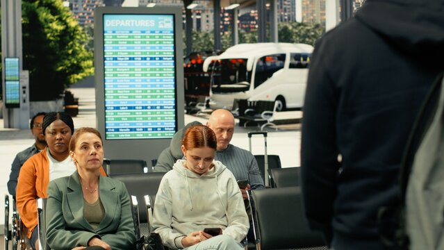Busy bus station with travelers waiting for express and sleeper bus routes, multicultural passengers with baggage sitting in waiting area before long-distance interstate journey.