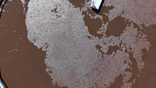 Brown water moves in shapes close to docks in a coastal area under sunlight. The scene shows a mix of water patterns and structures.