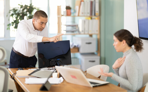 Young businessman of a large company, scolds his employee girl sitting at workdesk in the office