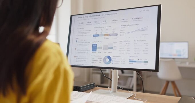 Woman analyst accountant reviews finance analytics report. She works at a computer monitor in an office, reviewing a spreadsheet with charts for budgeting. Finance analytics guide smart decisions.