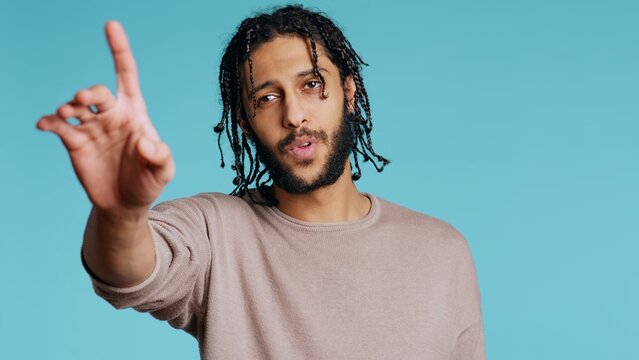 Assertive Middle Eastern man doing stop hand gestures. Annoyed BIPOC person doing firm halt sign gesturing, wishing to end concept, isolated over blue studio background, camera B