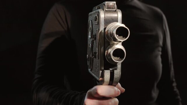 Retro vintage video camera in cameraman's hand on black background close-up, finger pressing trigger, filming recording started