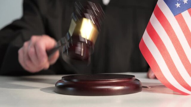 Judge hand striking gavel in courtroom with American flag on table, fair justice, crime and punishment, honest legislation