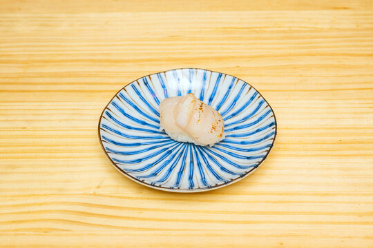 Grazing light from the side reveals the pearly texture of a freshly cut hotate (raw scallop) nigiri,